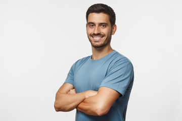 Portrait of attractive young sporty man in blue t-shirt standing with crossed arms isolated on gray...