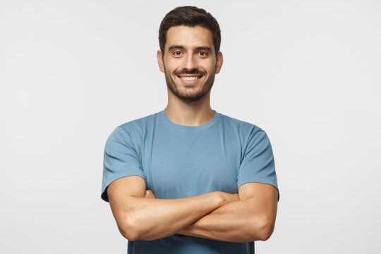 Smiling handsome man in blue t-shirt standing with crossed arms isolated on gray background