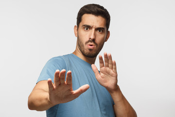 Young man showing stop gesture with both hands, wearin blue t-shirt, isolated on gray background