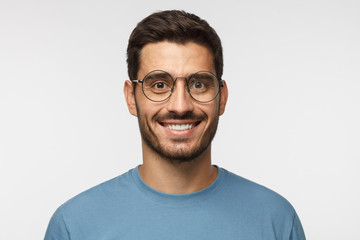 Obraz premium Close up shot of smiling attractive man in blue t-shirt and trendy round eyeglasses isolated on gray background