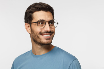 Closeup headshot of young man in round eyeglasses isolated on gray background, smiling happily,...