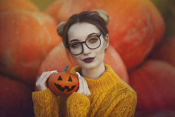 A cozy autumn photo of a girl with pumpkins in a yellow sweater and glasses. Stylish young woman in...