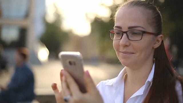 beautiful business lady with glasses in the Park looks through the photos on the smartphone screen