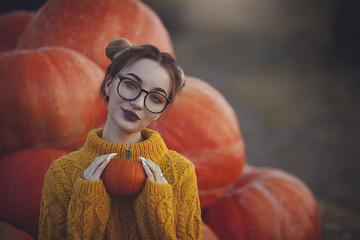 Cozy autumn photo of a girl with pumpkins in a yellow sweater and glasses. Stylish young woman in...