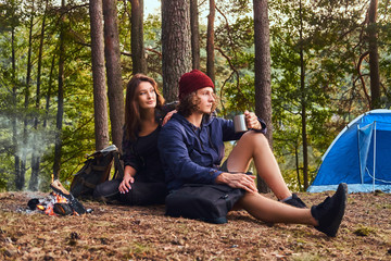 Portrait of a young couple - handsome curly guy and charming girl sitting together in the forest.