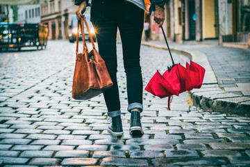 Woman with an umbrella and a purse goes across the street