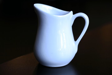 A close-up view of the top and side cups of coffee and a saucer and a jug with milk.
