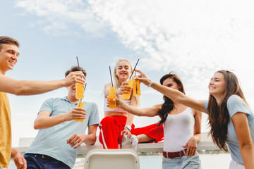 A company of good-looking friends laughing and drinking yellow cocktails in the nice cafe next to the river. Cheers. Entertainment, having good time. River is in the background.