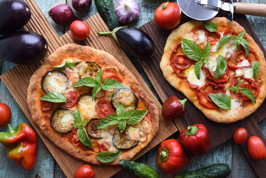 Healthy vegetarian meal. Homemade pizzas with aubergines, bell peppers, mozarella, basil and tomatoes on oak boards with raw ingredients