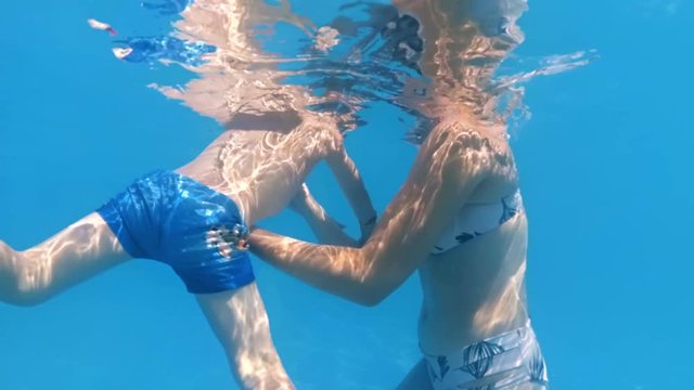 Slow motion underwater video of young mother supporting her little son swimming in pool at sunny day