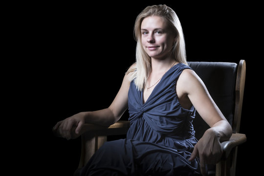 Portrait of a beautiful woman in a dress seated in an armchair isolated on a black background