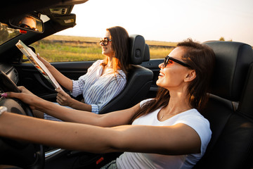 Beautiful dark-haired young women in sunglasses are sitting in a black cabriolet on a sunny day....