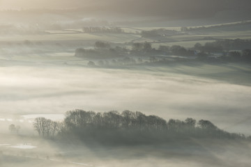 Stunning foggy English rural landscape at sunrise in Winter with layers rolling through the fields