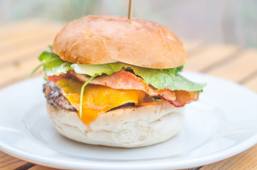 Cheeseburger from chopped beef cutlet with cheese, bacon, arugula and sauce on white plate.