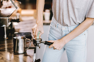 A good looking slim blonde with long hair,dressed in casual outfit,is cooking coffee in a modern coffee shop. Process of making coffee is shown.