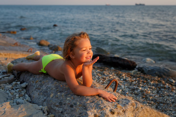 A little girl lies on a stone by the sea at sunset and dreams