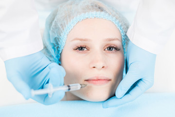 Young woman looking at camera while having lip filler injection in beauty salon