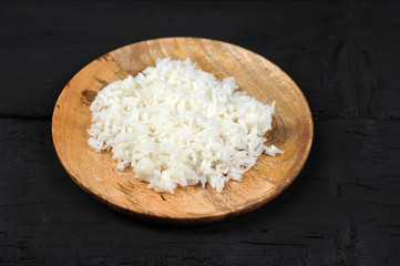 Boiled rice on a round wooden plate. View from above. Dark background. Close-up.