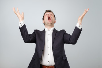 Portrait of excited young male in suit screaming in shock and amazement holding hands up.