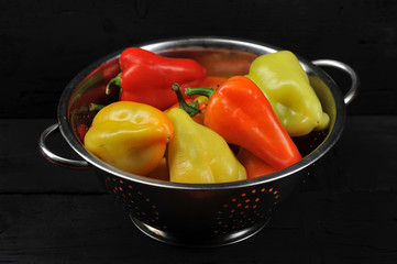 Pepper sweet Bulgarian in a deep bowl. Color of peppers is green, orange, red. Dark background. Close-up.