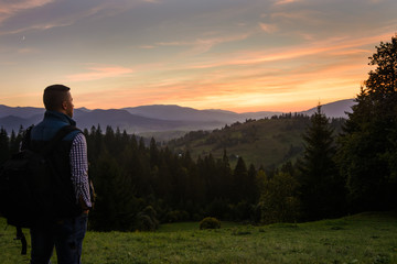 A tourist in the middle of the mountains looks at the sunset. Nature, travel, tourism