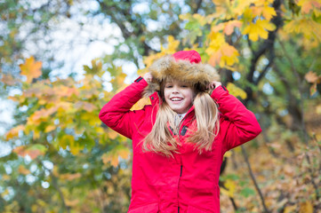 Hide above cozy hood or cape. Child blonde long hair walking in warm jacket outdoor. Girl happy in coat enjoy fall nature park. Child wear fashionable coat with hood. Fall clothes and fashion concept