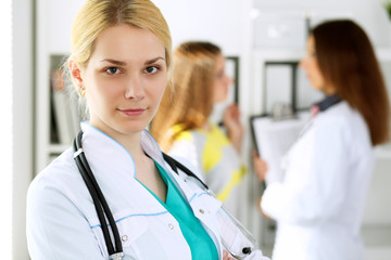 Doctor woman or nurse standing in a hospital office with her colleague in the background. Healthcare and medicine concept