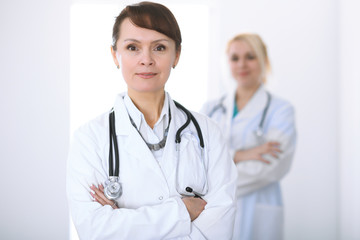 Fototapeta premium Female doctor standing with arms crossed in hospital. Medicine and health care concept