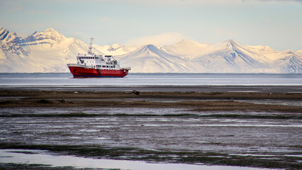 An icebreaker ship sits offshore in front of snow-covered mountains in Longyearbyen, Svalbard, Norwegian Arctic - obrazy, fototapety, plakaty