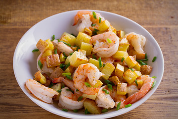 Shrimps with scallions and crispy potatoes in white bowl on wooden background. horizontal
