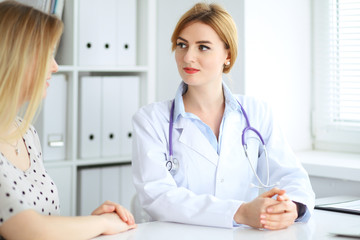 Doctor and patient discussing something while sitting at the desk at hospital. Medicine and health care concept