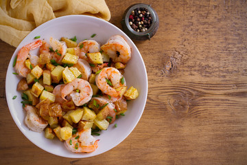Shrimps with scallions and crispy potatoes in white bowl on wooden background. overhead, horizontal