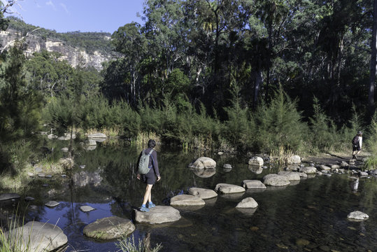 Female, baby boomer, hikers using stepping stones to cross the Carnarvon River in Carnarvon Gorge, Queensland, Australia.