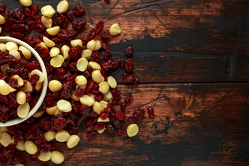 Healthy snack of Dried cranberries and macadamia nuts in a ceramic bowl on rustic wooden table