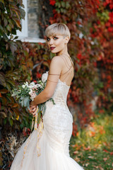 Fototapeta na wymiar portrait of a stylish bride with short hair on a background of a wall made of autumn leaves