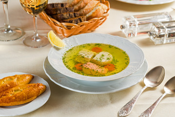 Fish soup with vegetables and spices in a white plate on a table with a tablecloth with bread and rolls