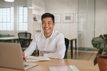 Smiling young Asian businessman working at his office desk