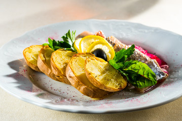 Herring with potatoes decorated with herbs with lemon and olive, cold appetizers for alcoholic beverages
