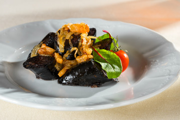 Homemade blood sausage with meat and porridge and pork blood. Bloody veal sausage. French cuisine: cooked baked blood sausage with onion on a plate.