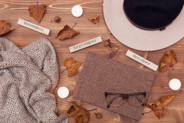Autumn composition. Flat lay, top view. Hat, scarf, glasses, bouquet of flowers, diary, candles, leaves on a wooden background with space for text 