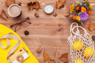 Fototapeta na wymiar Autumn composition. Flat lay, top view. Warm sweater, glasses, a bouquet of flowers, a camera, coffee, candles, knitted string bag of lemons and leaves on a wooden background with place for text