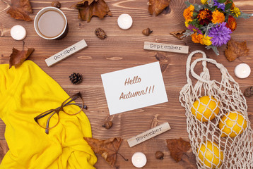 Autumn composition. Flat lay, top view. Warm sweater, glasses, a bouquet of flowers, coffee, candles, knitted string bag of lemons and yellow leaves on a wooden background