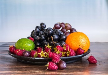 Delicious fruits salad in plate on table, lime, raspberry, grapes