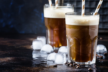 Cold frappe coffee with ice and foam in large glasses on brown background, selective focus