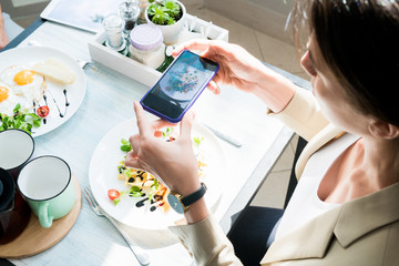 High angle portrait of unrecognizable young woman taking photo of beautiful food via smartphone while enjoying lunch in cafe, copy space