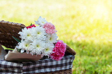 Flowers in picnic basket on the green grass nature background with sunlight.