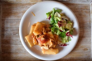 Pasta with meat tomato sauce and salad of green vegetables on a white plate
