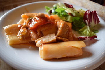 Pasta with meat tomato sauce and salad of green vegetables on a white plate