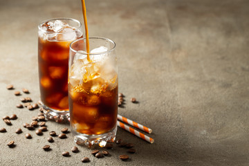 Ice coffee in a tall glass with cream poured over and coffee beans. Cold summer drink on a brown rusty background with copy space