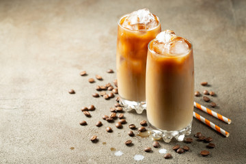 Ice coffee in a tall glass with cream poured over and coffee beans. Cold summer drink on a brown...